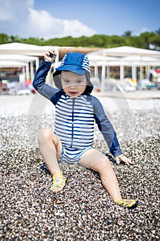 Toddler boy in a swimming suit plays with pebbles on the seashore in a hotel