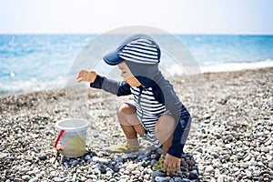 Toddler boy in a swimming suit plays with pebbles on the seashore in a hotel