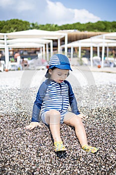 Toddler boy in a swimming suit plays with pebbles on the seashore in a hotel