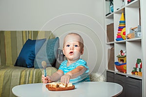 Toddler boy at table eating pie slices close-up and copy space. Baby with spoon and first lure