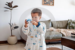 Toddler boy taking pictures with blue kids camera at home