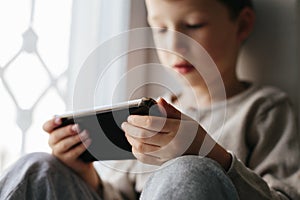 Toddler boy using tablet or smartphone. Cute five years old boy sitting at home using digital device.