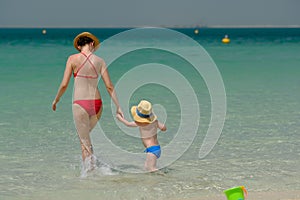 Toddler boy walking on beach with mother