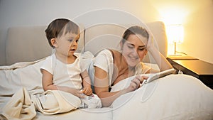 Adorable toddler boy watching as his mother using digital tablet in bed