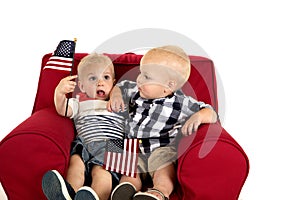 Toddler boys sitting in a red chair holding American flags