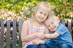 Toddler Brother and Sister Embrace On a Bench At The Park