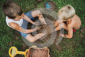 Toddler brothers sitting in a grass having fun playing with mud