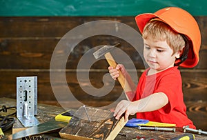 Toddler on busy face plays with hammer tool at home in workshop. Child in helmet cute playing as builder or repairer