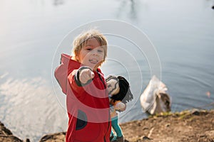 Toddler child, blond boy, standing on the edge of a lake, looking at swan