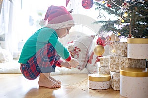 Toddler child, cute blond boy, sitting on the window in pajama, looking out for Satna Claus, Christmas lights around him