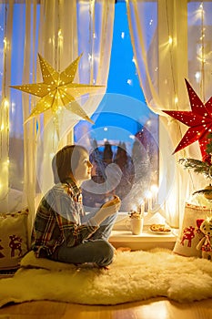 Toddler child, cute blond boy, sitting on the window in pajama, looking out for Satna Claus, Christmas lights around him