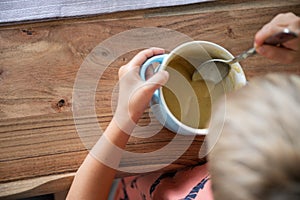 Toddler child eating creamed soup on wooden dinning table