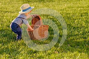 Toddler child outdoors. One year old baby boy wearing straw hat looking in picnic basket