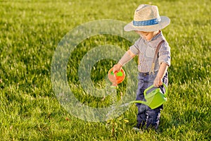 Toddler child outdoors. One year old baby boy wearing straw hat using watering can