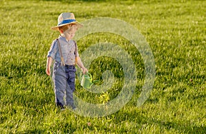 Toddler child outdoors. One year old baby boy wearing straw hat using watering can