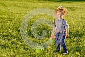 Toddler child outdoors. One year old baby boy wearing straw hat using watering can