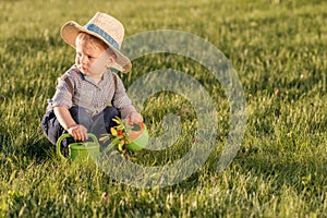 Toddler child outdoors. One year old baby boy wearing straw hat using watering can