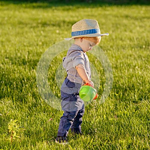 Toddler child outdoors. One year old baby boy wearing straw hat using watering can