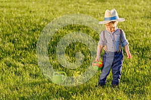 Toddler child outdoors. One year old baby boy wearing straw hat using watering can