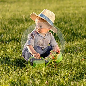 Toddler child outdoors. One year old baby boy wearing straw hat using watering can
