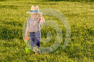 Toddler child outdoors. One year old baby boy wearing straw hat using watering can