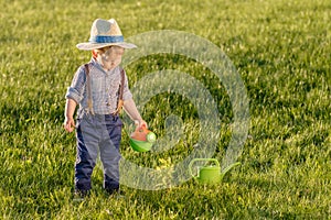 Toddler child outdoors. One year old baby boy wearing straw hat using watering can