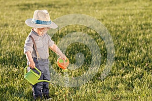 Toddler child outdoors. One year old baby boy wearing straw hat using watering can