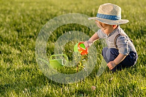 Toddler child outdoors. One year old baby boy wearing straw hat using watering can