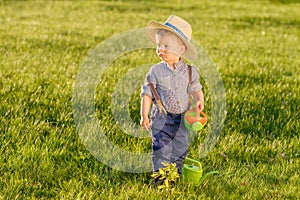 Toddler child outdoors. One year old baby boy wearing straw hat using watering can