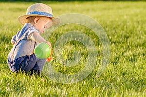 Toddler child outdoors. One year old baby boy wearing straw hat using watering can