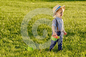 Toddler child outdoors. One year old baby boy wearing straw hat using watering can