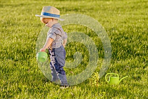 Toddler child outdoors. One year old baby boy wearing straw hat using watering can