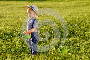 Toddler child outdoors. One year old baby boy wearing straw hat using watering can