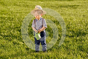 Toddler child outdoors. One year old baby boy wearing straw hat using watering can