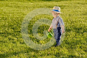 Toddler child outdoors. One year old baby boy wearing straw hat using watering can