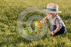 Toddler child outdoors. One year old baby boy wearing straw hat using watering can