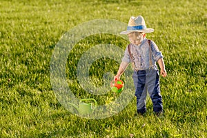 Toddler child outdoors. One year old baby boy wearing straw hat using watering can