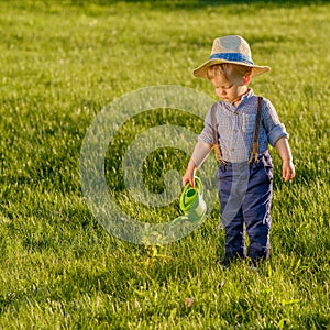 Toddler child outdoors. One year old baby boy wearing straw hat using watering can