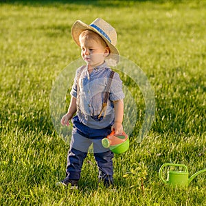 Toddler child outdoors. One year old baby boy wearing straw hat using watering can