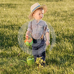 Toddler child outdoors. One year old baby boy wearing straw hat using watering can