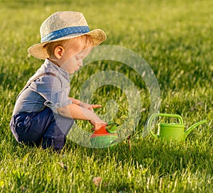 Toddler child outdoors. One year old baby boy wearing straw hat using watering can