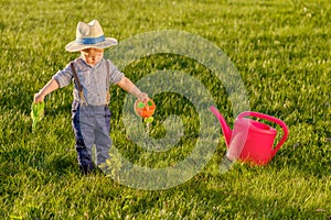 Toddler child outdoors. One year old baby boy wearing straw hat using watering can