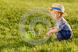 Toddler child outdoors. One year old baby boy wearing straw hat using watering can