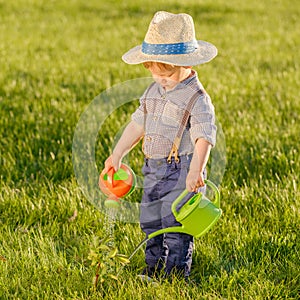 Toddler child outdoors. One year old baby boy wearing straw hat using watering can