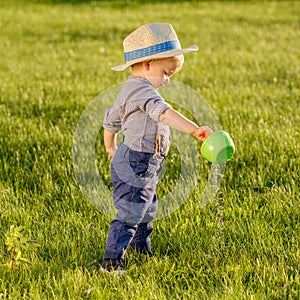 Toddler child outdoors. One year old baby boy wearing straw hat using watering can