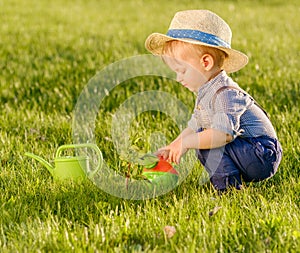 Toddler child outdoors. One year old baby boy wearing straw hat using watering can