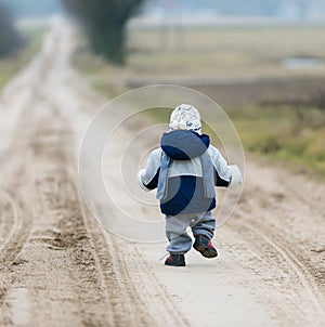 Toddler child walking by rural sandy road