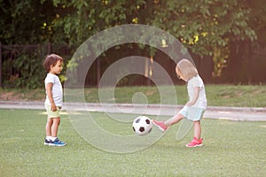 Toddler children, boy and girl, playing soccer together at football field. Little friends kicking ball in summer day outdoors