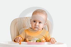 Toddler does not like vegetarian food, the child sitting on a feeding chair refuses to eat boiled vegetables