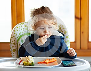 Toddler eats while watching movies on the mobile phone